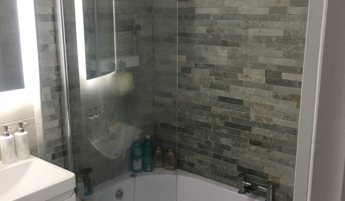 Backlit mirror next to a power shower surrounded by grey slate wall tiles