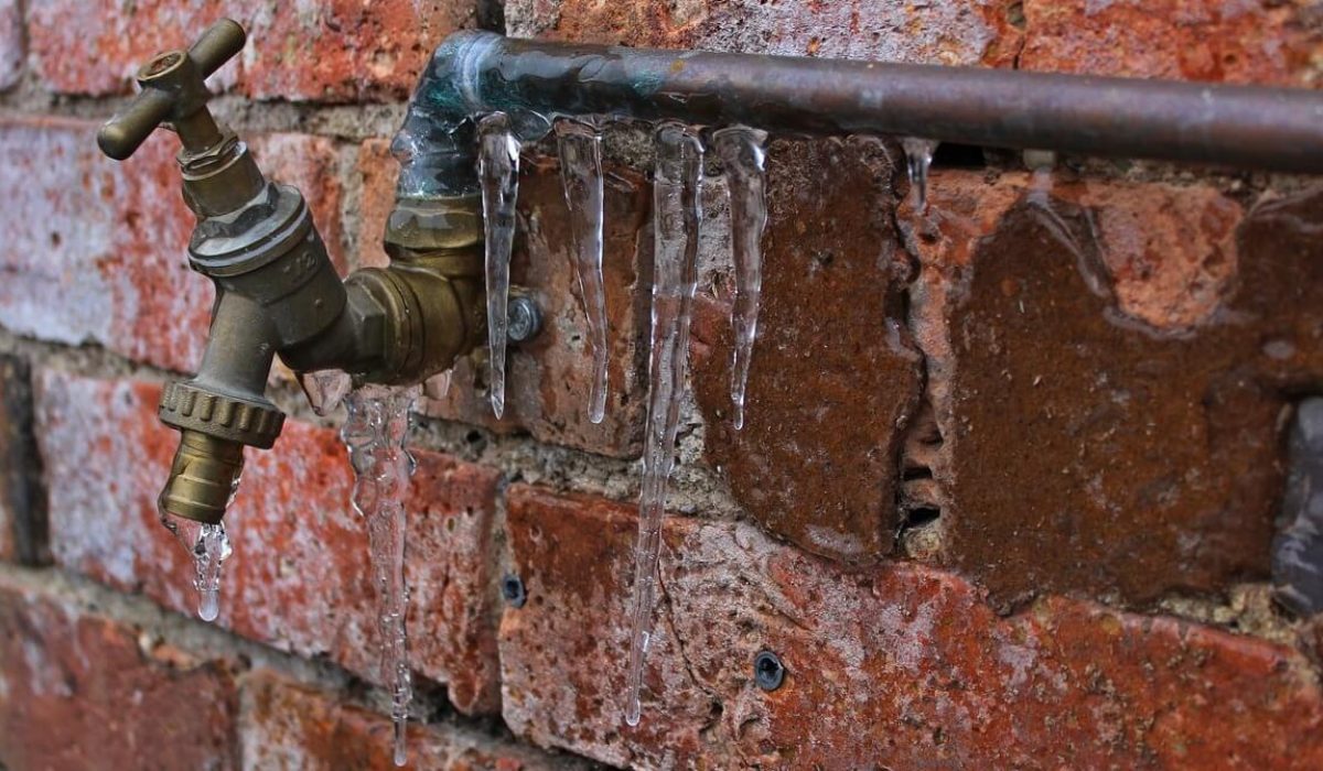 Red brick wall with a metal frozen pipe and tap attached with icicles hanging off it